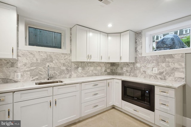 kitchen featuring white cabinets, sink, black microwave, and tasteful backsplash