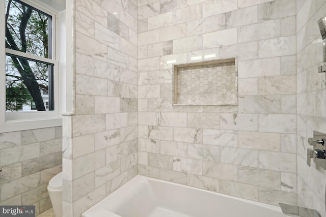 bathroom featuring tiled shower / bath, toilet, and tile walls