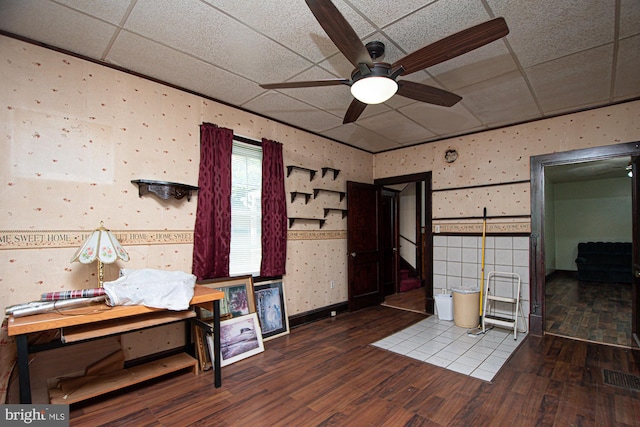 interior space featuring tile walls, ceiling fan, a drop ceiling, and wood-type flooring