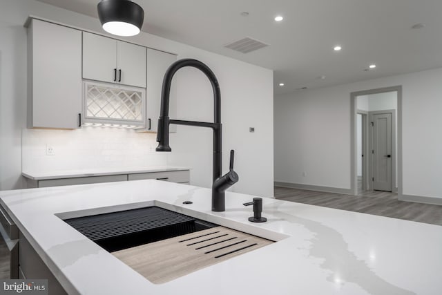 kitchen with white cabinets, light stone counters, backsplash, and wood-type flooring