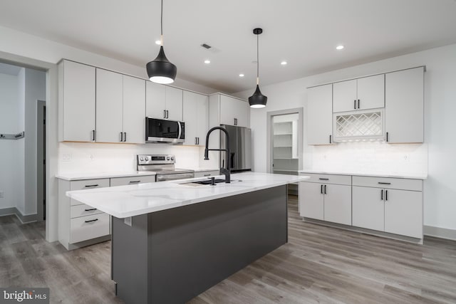 kitchen with stainless steel appliances, an island with sink, hardwood / wood-style flooring, and tasteful backsplash