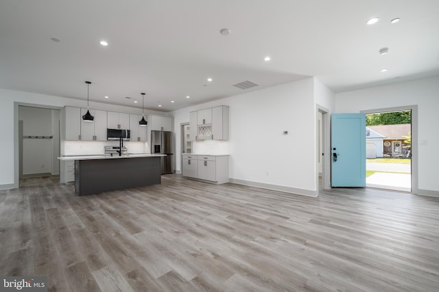 kitchen with decorative light fixtures, an island with sink, light wood-type flooring, appliances with stainless steel finishes, and sink