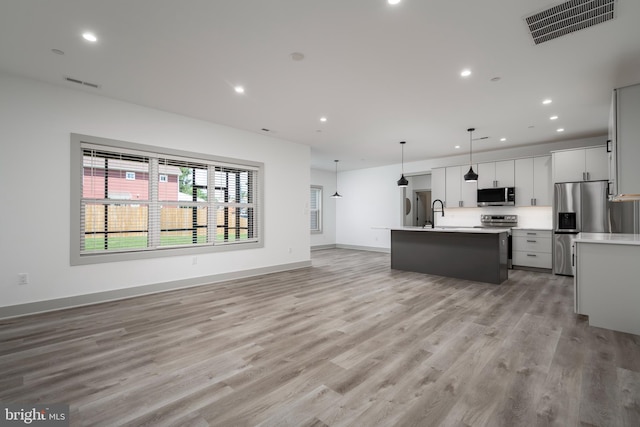 kitchen featuring light hardwood / wood-style floors, white cabinetry, an island with sink, appliances with stainless steel finishes, and pendant lighting