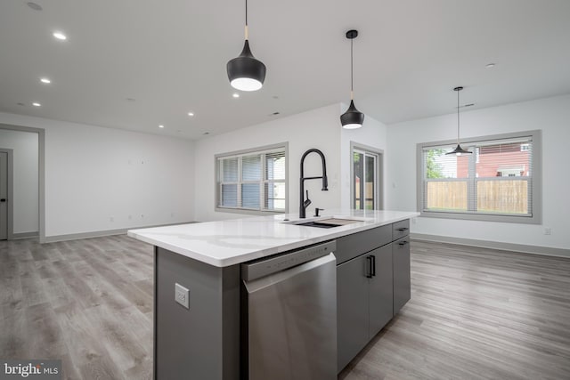 kitchen with hanging light fixtures, an island with sink, stainless steel dishwasher, light wood-type flooring, and sink