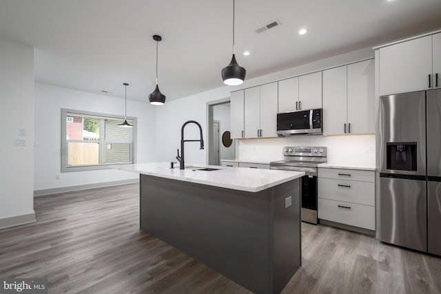 kitchen with light hardwood / wood-style flooring, stainless steel appliances, backsplash, a center island with sink, and sink