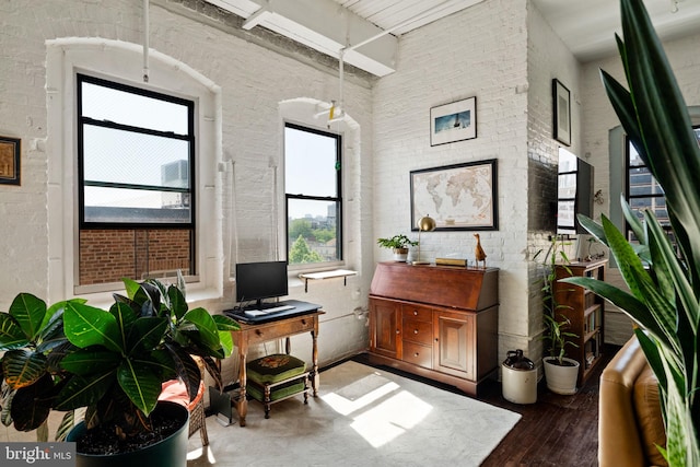 office space featuring a towering ceiling, brick wall, and wood-type flooring