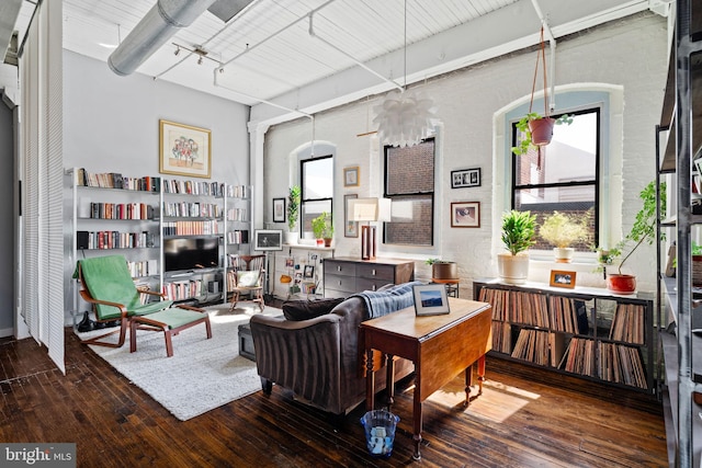 living room with rail lighting, dark wood-type flooring, and brick wall