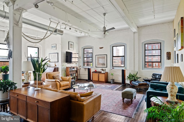 living room featuring beam ceiling, ceiling fan, brick wall, track lighting, and hardwood / wood-style flooring