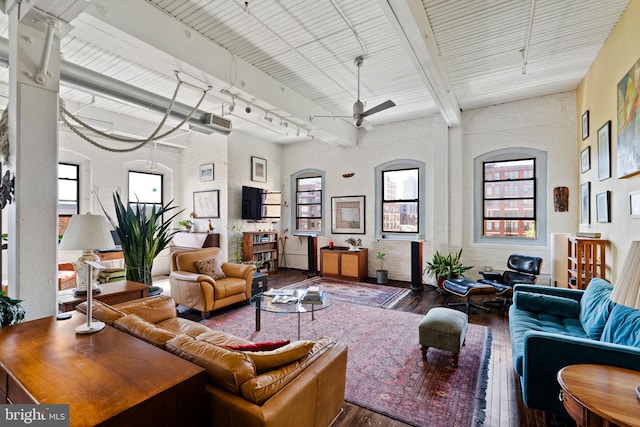 living room featuring beam ceiling, ceiling fan, rail lighting, a high ceiling, and hardwood / wood-style floors