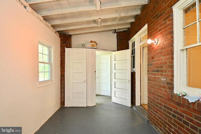 interior space with brick wall, concrete floors, and beam ceiling