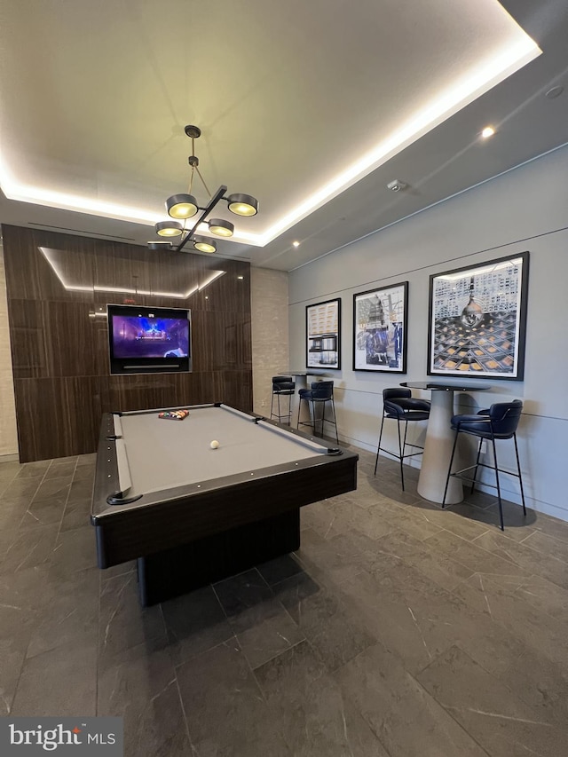 rec room featuring a notable chandelier, wood walls, a raised ceiling, and pool table