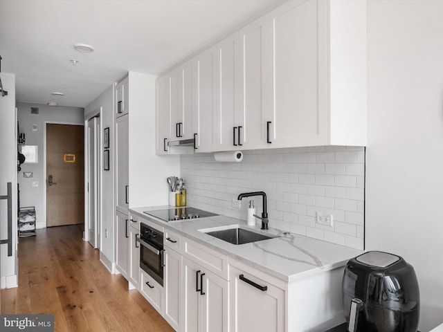 kitchen with black electric stovetop, wall oven, white cabinetry, and sink