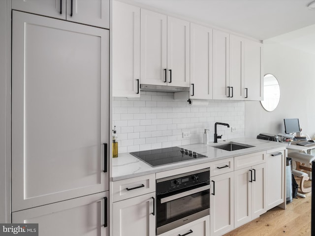 kitchen featuring stainless steel oven, white cabinets, paneled refrigerator, black electric cooktop, and light stone counters