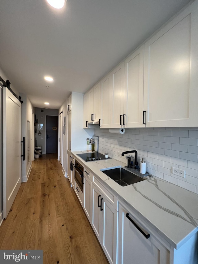 kitchen featuring white cabinetry, sink, a barn door, light stone counters, and light wood-type flooring