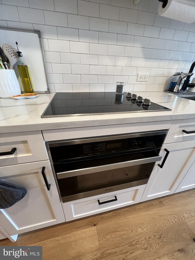 details with light stone countertops, backsplash, black appliances, light hardwood / wood-style floors, and white cabinetry