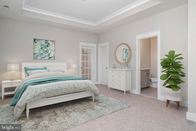 carpeted bedroom featuring a tray ceiling and ensuite bath