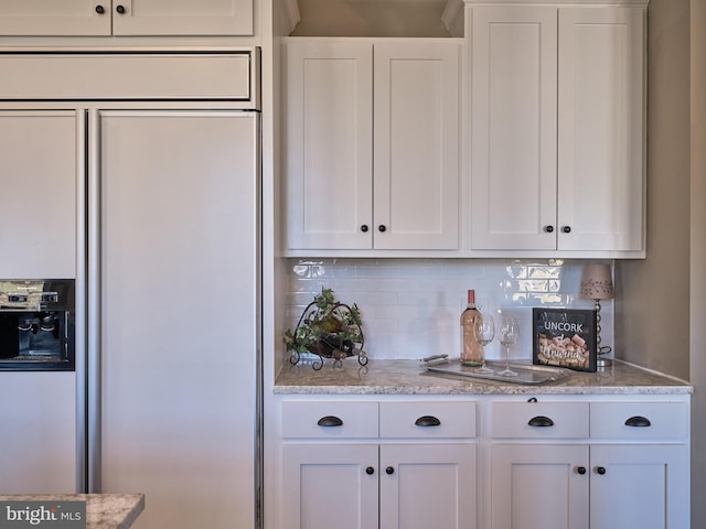 kitchen featuring paneled built in refrigerator, light stone counters, tasteful backsplash, and white cabinetry