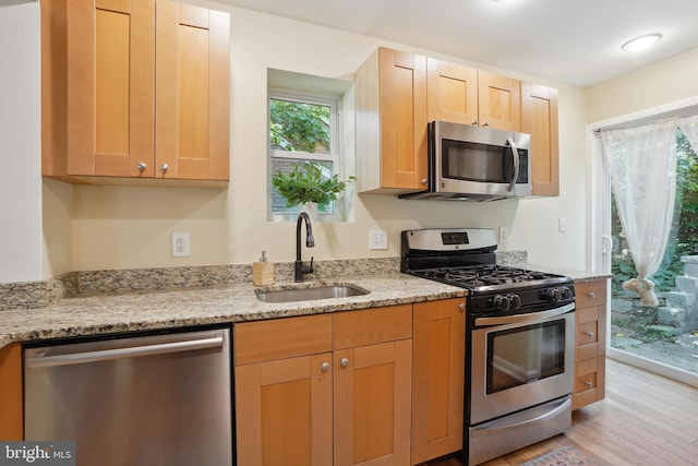 kitchen with light stone countertops, sink, light brown cabinets, light hardwood / wood-style flooring, and appliances with stainless steel finishes