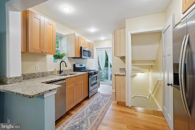 kitchen featuring light stone countertops, sink, a healthy amount of sunlight, stainless steel appliances, and light hardwood / wood-style floors