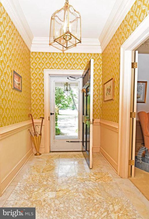 doorway with tile flooring, ornamental molding, and a chandelier