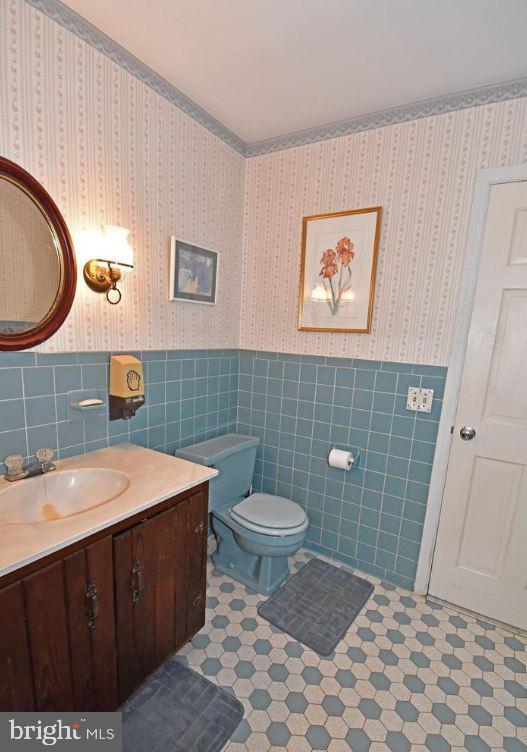 bathroom with tile flooring, tile walls, toilet, and vanity