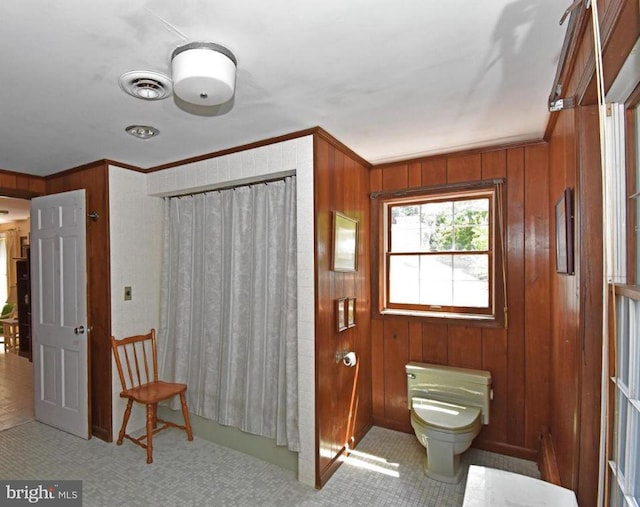 bathroom featuring tile floors, wooden walls, crown molding, and toilet