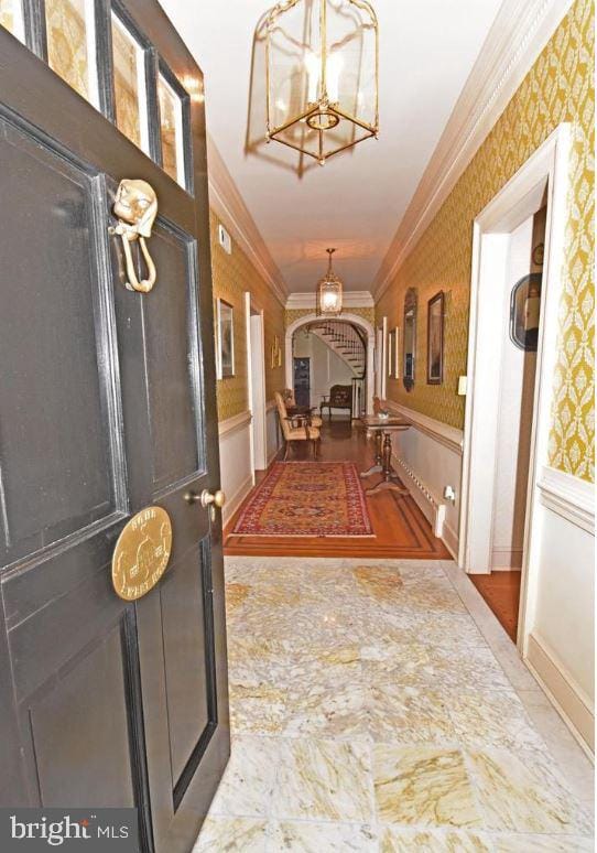 hall with tile flooring, a notable chandelier, and ornamental molding