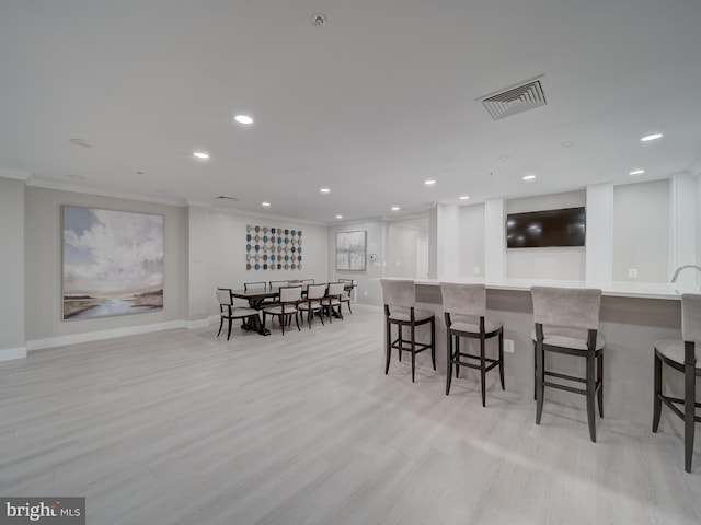 dining area featuring crown molding, indoor bar, and light hardwood / wood-style flooring