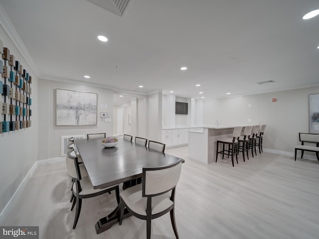 dining space featuring crown molding, bar, and light hardwood / wood-style flooring