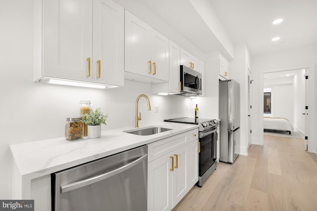 kitchen featuring light hardwood / wood-style flooring, light stone counters, sink, white cabinetry, and appliances with stainless steel finishes