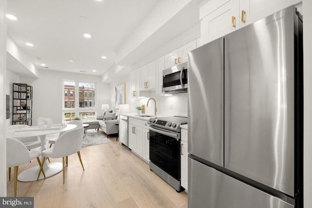 kitchen featuring appliances with stainless steel finishes, sink, white cabinets, and light wood-type flooring