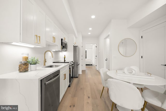 kitchen with light hardwood / wood-style flooring, appliances with stainless steel finishes, white cabinets, light stone counters, and sink