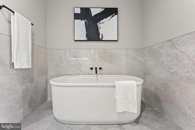 bathroom with tile floors, a bathtub, and tile walls