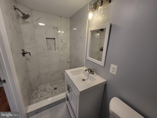 bathroom with tiled shower, tile flooring, large vanity, and toilet