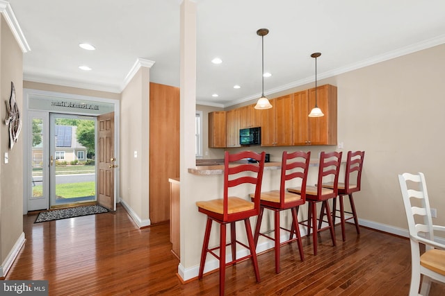 kitchen featuring hanging light fixtures, ornamental molding, a kitchen breakfast bar, and dark hardwood / wood-style flooring