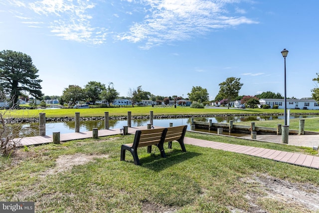 view of property's community featuring a water view, a dock, and a lawn