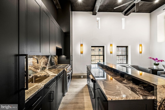 kitchen featuring light hardwood / wood-style floors, stone countertops, beam ceiling, backsplash, and stainless steel range