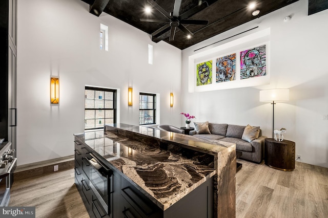 kitchen with light hardwood / wood-style floors, stone counters, a high ceiling, and ceiling fan