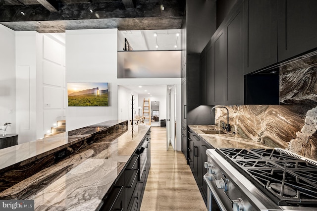 kitchen with stainless steel stove, backsplash, light stone countertops, light wood-type flooring, and sink