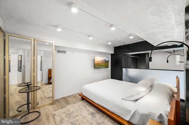 bedroom featuring track lighting, a textured ceiling, and light wood-type flooring