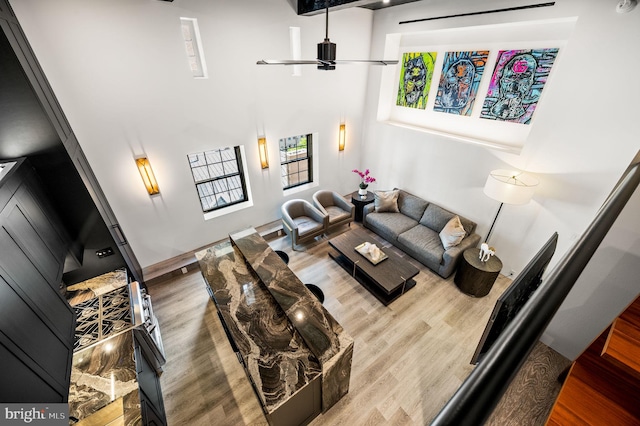 living room with a high ceiling, ceiling fan, and wood-type flooring