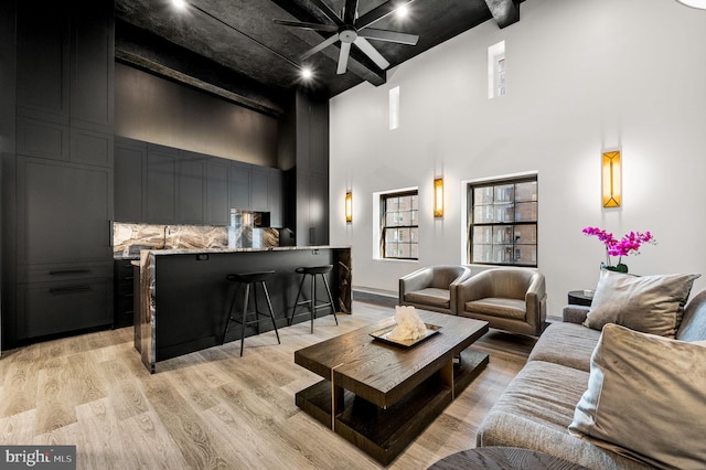 living room with ceiling fan, a towering ceiling, and light wood-type flooring