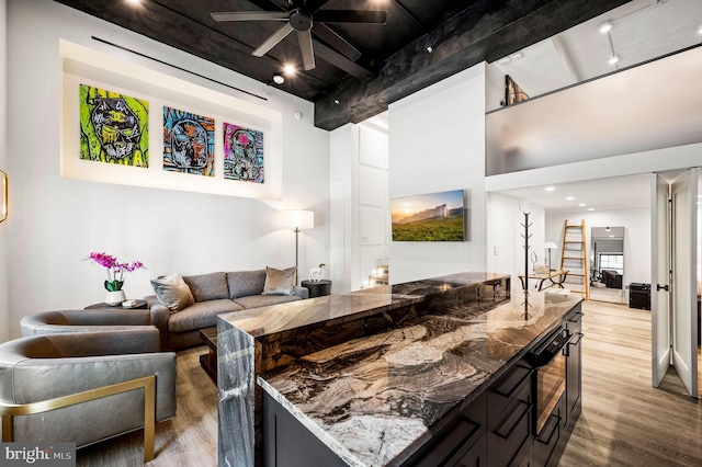 kitchen with ceiling fan, beamed ceiling, dark stone countertops, a high ceiling, and hardwood / wood-style flooring