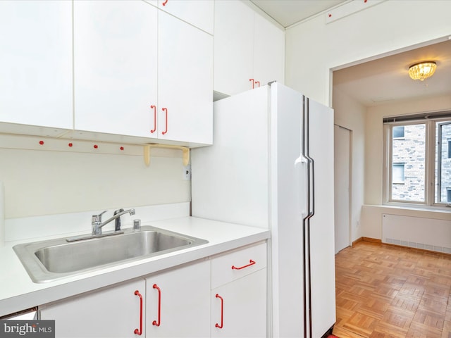 kitchen featuring white refrigerator, light parquet flooring, sink, white cabinetry, and radiator