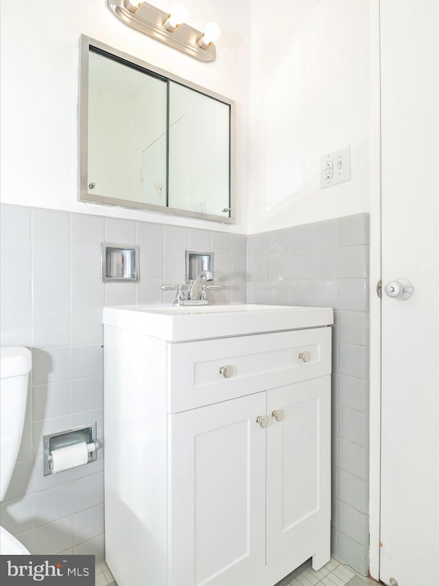 bathroom with tile floors, vanity, toilet, and tile walls