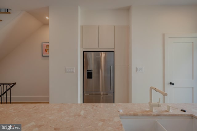 kitchen featuring light stone counters, stainless steel refrigerator with ice dispenser, and sink