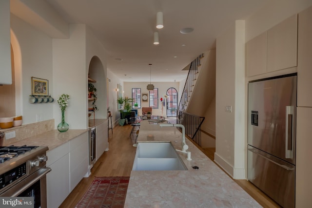 kitchen with white cabinets, stainless steel appliances, light wood-type flooring, decorative light fixtures, and sink