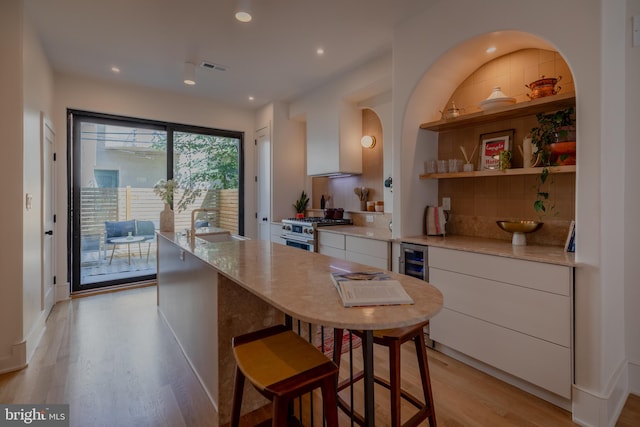 kitchen with white cabinets, beverage cooler, light wood-type flooring, and stainless steel range