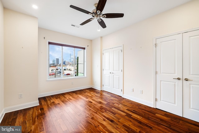 unfurnished bedroom featuring multiple closets, wood-type flooring, and ceiling fan