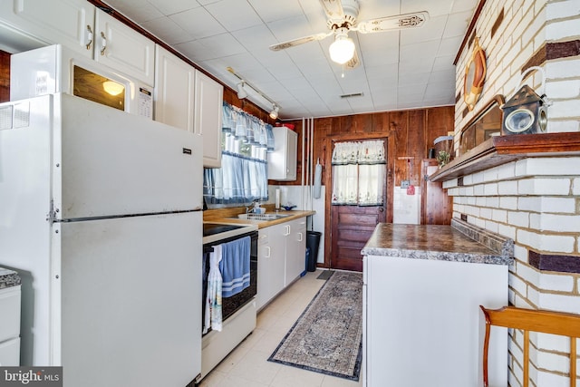 kitchen with ceiling fan, white appliances, light tile floors, wood walls, and white cabinetry